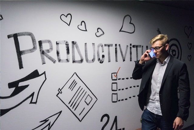 Das Bild zeigt einen telefonierenden Mann vor einem Whiteboard auf dem Productivity steht